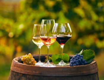 three glasses of different wines on a barrel with grape clusters flanking